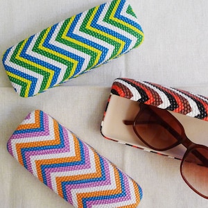 May include: Three colourful patterned eyeglass cases. Two cases are closed and one case is open with brown sunglasses inside.