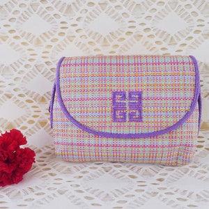 May include: A small, rectangular, purple and multi-coloured patterned cosmetic bag with a purple zipper and a purple embroidered logo that says "Givenchy".