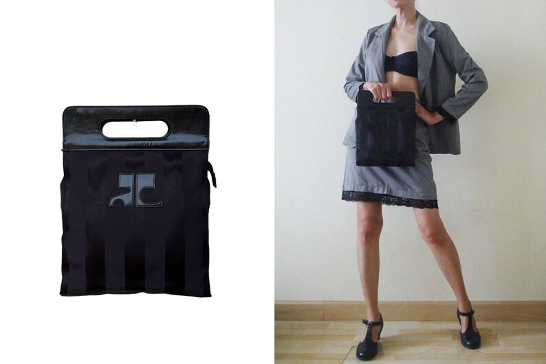 May include: Black tote bag with a handle and a rectangular shape. The bag has vertical stripes and a logo on the front. The top handle is black and shiny. The bag is shown next to a person wearing a gray suit.