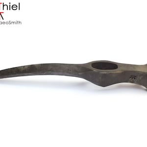 Op de afbeelding: Een gebogen, handgesmeed stalen bijlkop met een puntige punt en een gat voor een handvat. De bijlkop is gemaakt door AdiThiel, de Archaeosmith.