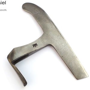 Peut inclure: Une hache en acier forgée à la main avec une lame incurvée unique et une finition texturée. La hache a un petit trou dans la poignée et la lame est décorée d'un motif.