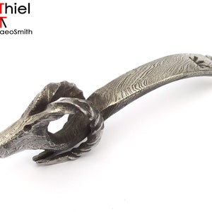 Op de afbeelding: Een zilveren metalen flessenopener in de vorm van een rammenkop met een gedraaide handgreep. De handgreep is gemaakt van gepatenteerd metaal.
