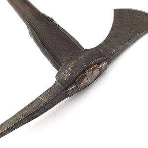 May include: A close-up of a vintage axe with a wooden handle and a metal head. The axe has a sharp blade and a pick on the opposite side. The axe is in good condition and has a rustic look.