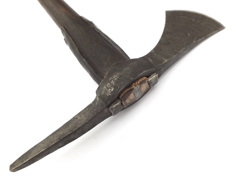 May include: A close-up of a vintage axe with a wooden handle and a metal head. The axe has a sharp blade and a pick on the opposite side. The axe is in good condition and has a rustic look.