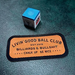 May include: A black and orange patch with the text "Livin' Good Ball Club Est 2019 Billiards & Bullshit Chalk Up Be Nice..." in white lettering. The patch has a geometric pattern of hexagons.