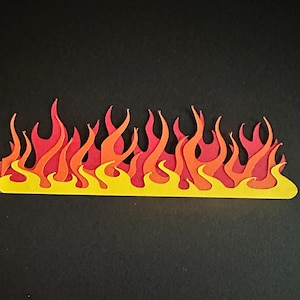 May include: A layered paper cutout of flames in shades of red, orange, and yellow. The flames are stylized with a jagged, uneven edge, and the base is a bright yellow. The background is a solid black.