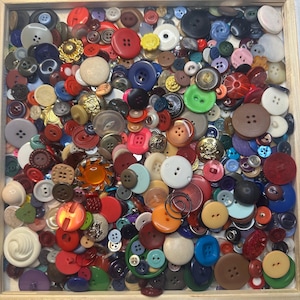 May include: A square wooden tray filled with a large collection of assorted sewing buttons in various colors, shapes, and sizes. The buttons include round, flat, and textured designs in shades of red, blue, green, brown, white, and black.