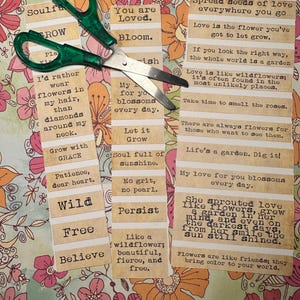 Puede incluir: Unas tijeras verdes descansan sobre un fondo floral, junto a varias etiquetas de papel con citas inspiradoras. Las etiquetas presentan frases como "You are Loved", "Bloom" y "Spread seeds of love". El tema general est&aacute; relacionado con la positividad y la naturaleza.