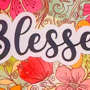 May include: A floral design with the word "Blessed" in a cursive font. The background features a variety of flowers in shades of pink, orange, and yellow, set against a light green backdrop. The artwork has a watercolor style.