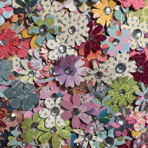 May include: A collection of colorful paper flowers with glitter and rhinestones. The flowers are in various shades of pink, blue, green, and purple.