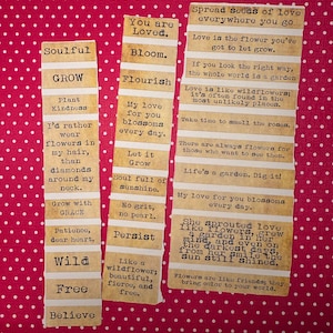 Puede incluir: Tres tiras de papel con citas y frases inspiradoras sobre un fondo rojo de lunares. Las frases incluyen "You are Loved", "Bloom", "Flourish", "Grow" y "Spread seeds of love everywhere you go."