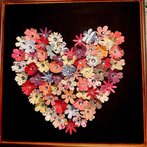 May include: A framed heart-shaped artwork made of colorful paper flowers with jeweled centers. The flowers are arranged in a heart shape on a black background.