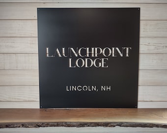 May include: Black metal sign with white cut-out lettering that reads "Launchpoint Lodge" and "Lincoln, NH".