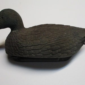 Puede incluir: Un se&ntilde;uelo de pato gris oscuro con marcas de plumas detalladas. El se&ntilde;uelo est&aacute; hecho de pl&aacute;stico y tiene un aspecto realista.