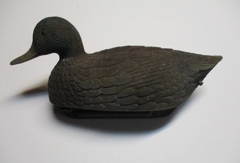 Puede incluir: Un se&ntilde;uelo de pato gris oscuro con marcas de plumas detalladas. El se&ntilde;uelo est&aacute; hecho de pl&aacute;stico y tiene un aspecto realista.