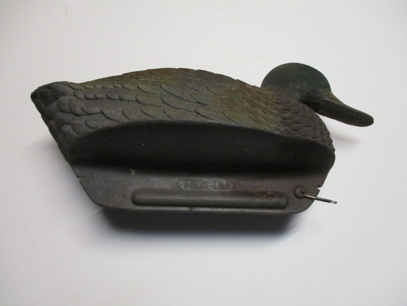 Puede incluir: Un se&ntilde;uelo de pato de pl&aacute;stico negro y verde con un dise&ntilde;o realista. El se&ntilde;uelo tiene un anillo de metal en la parte inferior y el texto "Clam-Dak" es visible en la parte inferior.