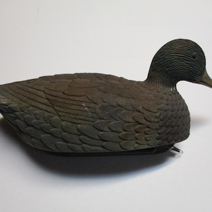 Puede incluir: Un se&ntilde;uelo de pato de pl&aacute;stico marr&oacute;n y negro con marcas de plumas detalladas. El se&ntilde;uelo est&aacute; dise&ntilde;ado para parecerse a un pato real y se utiliza para la caza.