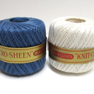 Op de afbeelding: Twee spoelen garen, één marineblauw en één wit, worden weergegeven tegen een witte achtergrond. Elke spoel is omwikkeld met een goud en rood label met de tekst "KNIT-CRO" en "CRO-SHEEN". Ideaal voor diverse knutselprojecten.