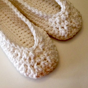 May include: A pair of white crocheted slippers. The slippers are made with a simple stitch and have a rounded toe.