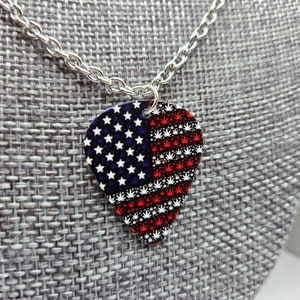 May include: A silver chain necklace with a guitar pick pendant. The pick is decorated with an American flag design featuring red, white, and blue stars and marijuana leaf patterns.