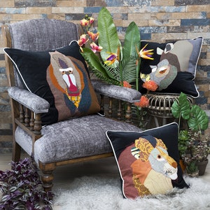 May include: Three decorative throw pillows with animal faces. The pillows are black with white trim and feature a baboon, a rhinoceros, and a lion. The pillows are on a gray armchair and a white rug.