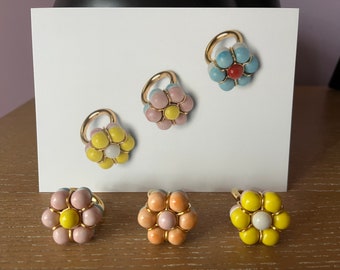 May include: Five gold rings with colorful flower designs. Each ring features a center circle surrounded by smaller circles in shades of yellow, pink, blue, and white.