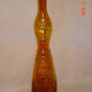 May include: A tall amber glass bottle with a face design on the neck and a diamond pattern on the body.