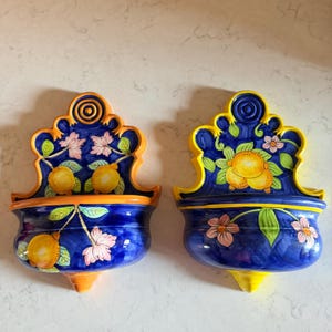May include: Two ceramic wall-mounted basins featuring a deep blue background with hand-painted yellow lemons, green leaves, and pink flowers. The left basin has an orange rim, while the right basin has a bright yellow rim and decorative scrollwork.