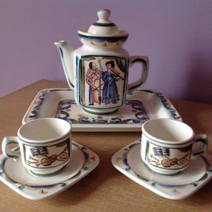 May include: A ceramic tea set with a teapot, two cups, and saucers. The teapot features a painted scene of two people playing music. The cups and saucers have a similar design with musical instruments.