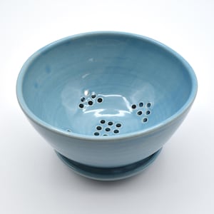 May include: A light blue ceramic colander with drainage holes. The colander sits on a matching base. The bowl has a smooth, glossy finish. This kitchenware is ideal for washing and draining fruits and vegetables.