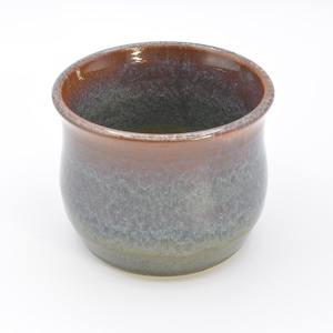May include: A handmade ceramic cup with a rounded shape. The cup has a gradient color scheme, transitioning from a dark brown rim to a gray-green body. The interior is a darker shade of gray.