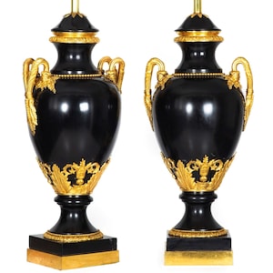 May include: A pair of black and gold table lamps with ornate details. The lamps are made of black marble and have gold accents. The bases are square and the shades are missing.