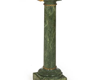 May include: A green marble pedestal with gold accents. The pedestal has a square base and a round top.