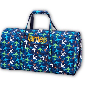 Pu&ograve; includere: Una borsa da viaggio blu con un motivo ripetuto di aerei bianchi, verdi, blu e arancioni. La borsa ha una tracolla e manici. Il nome "James" &egrave; ricamato in giallo sul davanti.