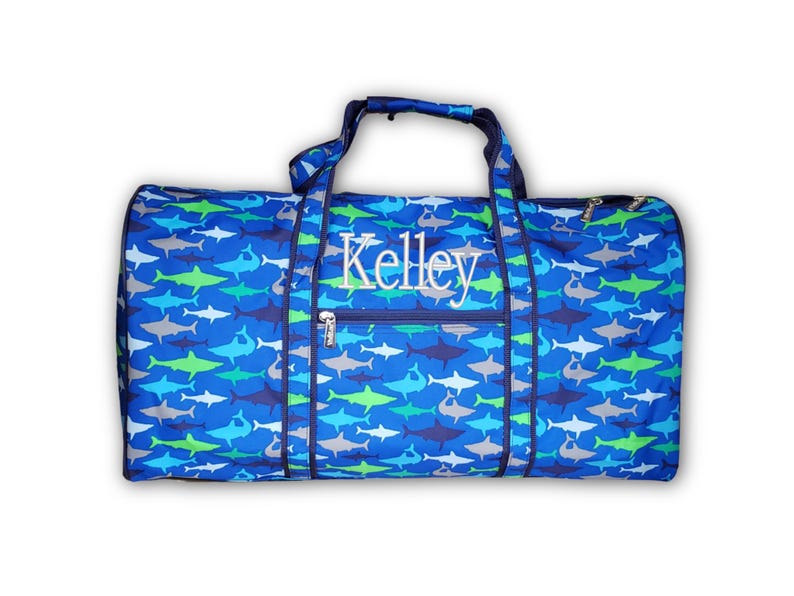 Pu&ograve; includere: Una borsa da viaggio blu con un motivo a squali nei toni del blu, verde e grigio. La borsa ha una tasca frontale con cerniera e manici. Il nome "Kelley" &egrave; ricamato sul davanti.