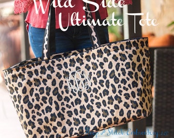 May include: A large tote bag with a leopard print pattern in tan, brown, and black. The bag has black handles and trim, and features the text "Wild Side Ultimate Tote" in white. A monogram is embroidered on the front.