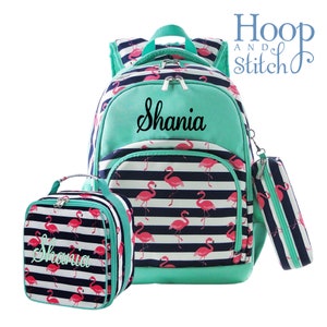 May include: A turquoise and black striped backpack with pink flamingos, a matching lunch bag, and a pencil case. The backpack has a large front pocket with the name "Shania" embroidered on it. The lunch bag and pencil case also have the name "Shania" embroidered on them.