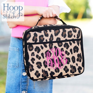 May include: A brown and black leopard print insulated lunch bag with a black zipper and a pink monogram "BBE".