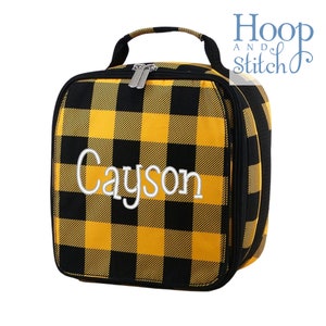 Op de afbeelding: Gele en zwarte geruite lunchtas met een ritssluiting en een handvat. De tas is gepersonaliseerd met de naam "Cayson" in witte borduurwerk.