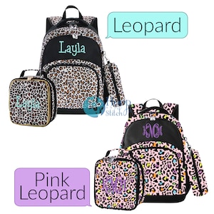 May include: Two sets of leopard print backpacks, lunch bags, and pencil pouches. The first set is brown and black with the name "Layla" embroidered on the backpack. The second set is pink with a multi-colored leopard print and the monogram "K.M.M." embroidered on the backpack.