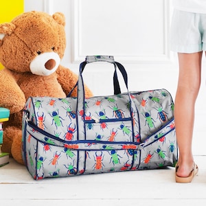 Pu&ograve; includere: Borsa da viaggio grigia con un motivo di insetti colorati. La borsa ha finiture, manici e cerniera blu navy. Un grande orsacchiotto marrone &egrave; sullo sfondo. Ideale per viaggiare o trasportare oggetti.