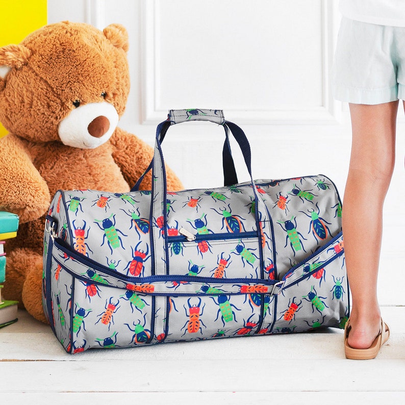 Pu&ograve; includere: Borsa da viaggio grigia con un motivo di insetti colorati. La borsa ha finiture, manici e cerniera blu navy. Un grande orsacchiotto marrone &egrave; sullo sfondo. Ideale per viaggiare o trasportare oggetti.