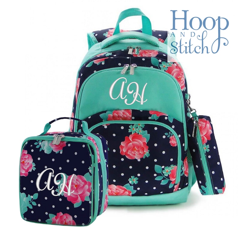May include: A teal and navy blue floral backpack set with a lunch bag and pencil pouch. The backpack has a large front pocket with a teal zipper and the initials "AJ" embroidered in white. The lunch bag and pencil pouch have the same floral pattern and the initials "AJ" embroidered in white.