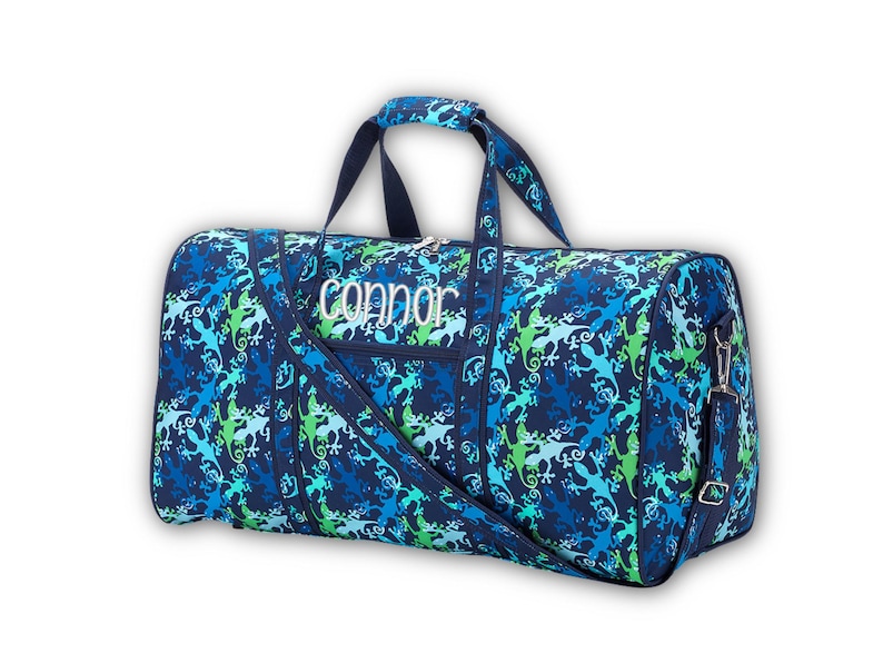 Pu&ograve; includere: Borsa da viaggio blu con un motivo a lucertola nei toni del blu e del verde. La borsa ha un manico superiore, una tracolla e il nome "Connor" ricamato in bianco. La borsa misura circa 61 cm di lunghezza.