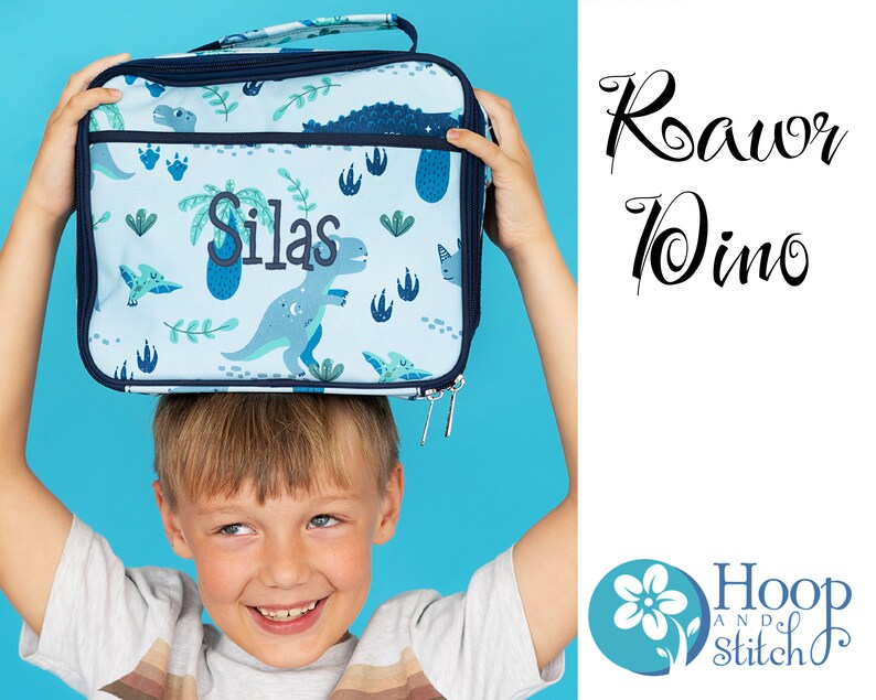 May include: A blue lunch bag with a dinosaur print and the name "Silas" embroidered on it. The bag is being held up by a child. The text "Roar Dino" is written in black cursive on a white background. The logo for "Hoop and Stitch" is in the bottom right corner.
