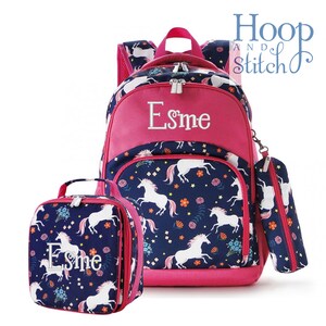 May include: A pink and blue unicorn-themed backpack set with a lunch bag and pencil case. The backpack has a pink front pocket with the name "Esme" embroidered on it. The lunch bag and pencil case have the same unicorn pattern as the backpack.