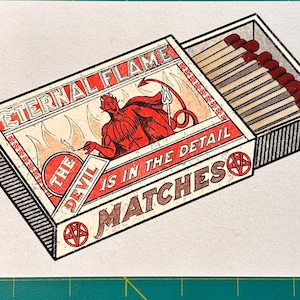 Könnte beinhalten: Eine Streichholzschachtel im Vintage-Stil mit dem Text "ETERNAL FLAME" und "THE DEVIL IS IN THE DETAIL MATCHES". Die Schachtel zeigt eine rote Teufelsillustration und enthält Streichhölzer mit roten Köpfen. Das Design ist retro.