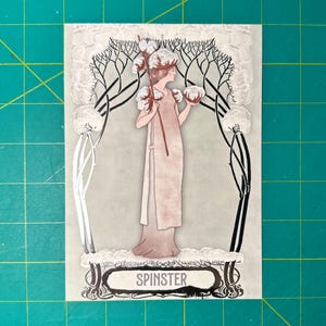 May include: A vintage art nouveau style illustration of a woman standing in a field of cotton. The woman is wearing a long white dress and holding a branch of cotton. The illustration is in shades of gray, white, and black. The text "SPINSTER" is printed below the illustration.