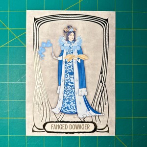 May include: Illustration of a woman in a blue and white patterned dress and cape, holding a blue object and a fan. The image is framed with black lines and the text "FANGED DOWAGER" is at the bottom.