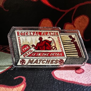 May include: A red and black matchbox with a clear plastic cover. The matchbox has a red devil illustration with the text "The Devil is in the Detail" and "Eternal Flame Matches".